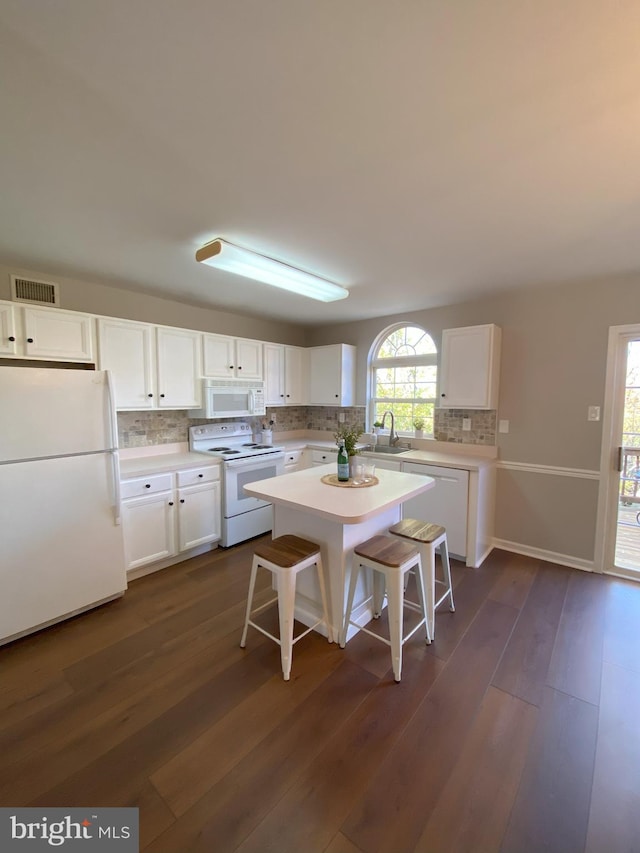 kitchen with white appliances, dark wood-type flooring, white cabinetry, light countertops, and a kitchen bar