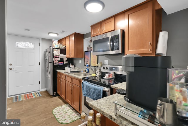 kitchen with stainless steel appliances, light stone countertops, sink, and light wood-type flooring