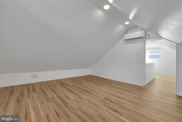 additional living space featuring a wall unit AC, light hardwood / wood-style floors, and vaulted ceiling