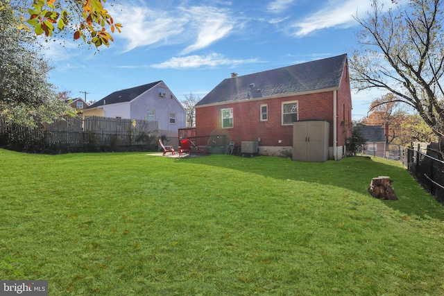 back of house with central AC, a yard, and a storage unit