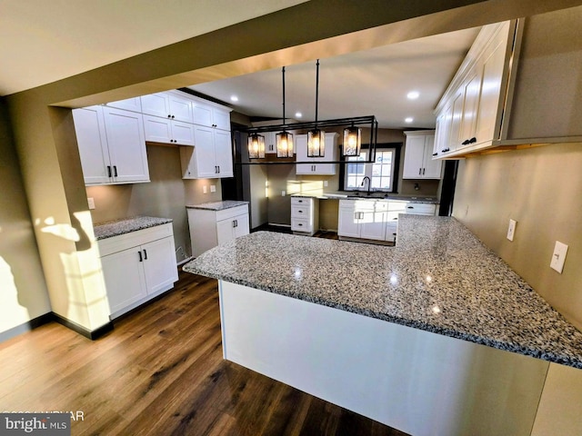 kitchen with dark stone counters, white cabinetry, dark hardwood / wood-style floors, hanging light fixtures, and sink