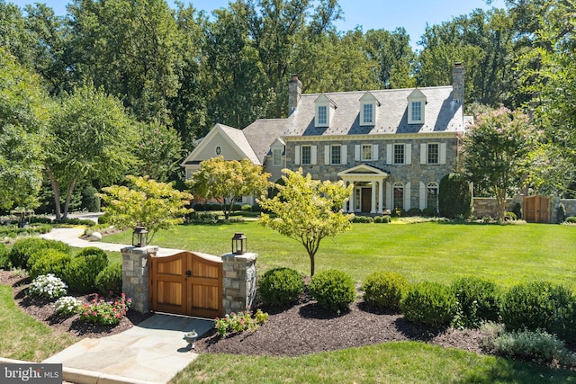 view of front of house featuring stone siding, a chimney, a gate, fence, and a front lawn