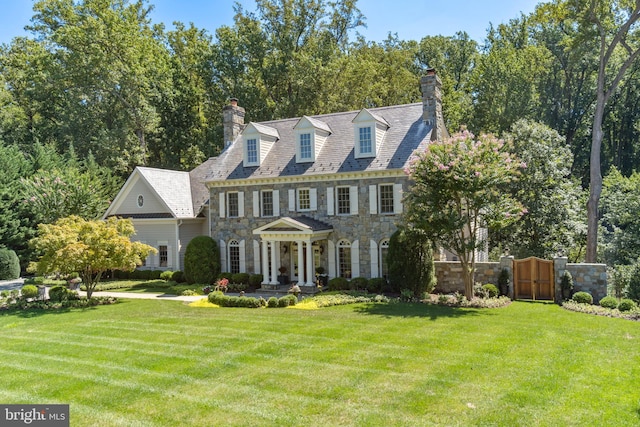 colonial home with stone siding, fence, a front lawn, and a gate