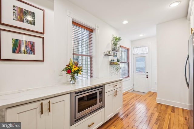 kitchen featuring light hardwood / wood-style floors, light stone counters, white cabinetry, and appliances with stainless steel finishes