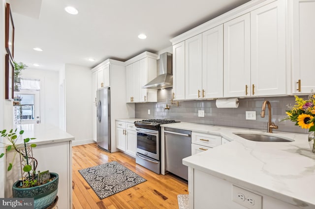 kitchen featuring white cabinetry, light wood-type flooring, wall chimney range hood, and appliances with stainless steel finishes