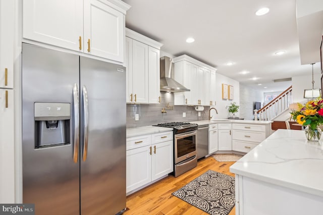 kitchen with wall chimney exhaust hood, light hardwood / wood-style floors, white cabinetry, and appliances with stainless steel finishes