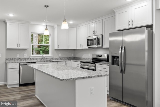 kitchen with appliances with stainless steel finishes, decorative light fixtures, hardwood / wood-style floors, a center island, and white cabinetry