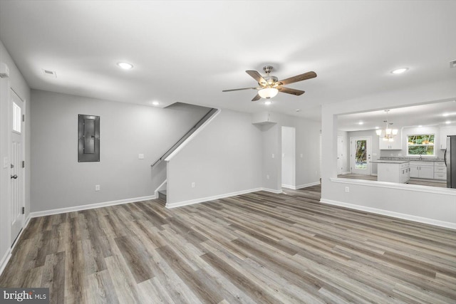 unfurnished living room featuring ceiling fan with notable chandelier, light wood-type flooring, and electric panel