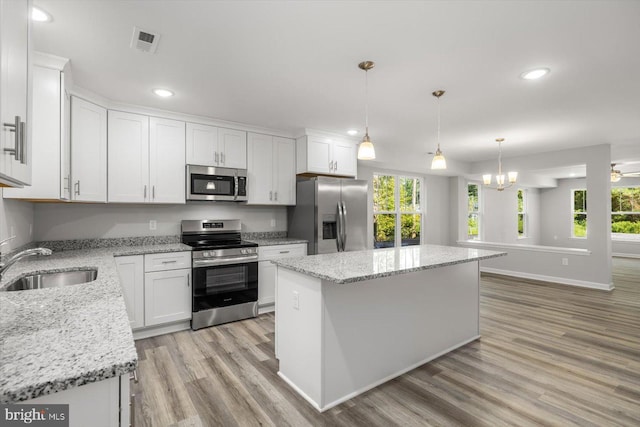 kitchen featuring a center island, sink, hanging light fixtures, white cabinetry, and stainless steel appliances