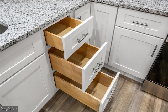 details featuring light stone countertops, hardwood / wood-style floors, and white cabinets