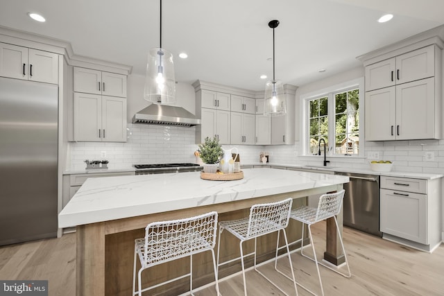 kitchen featuring stainless steel appliances, sink, decorative light fixtures, light hardwood / wood-style flooring, and a kitchen island