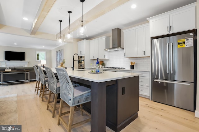 kitchen with stainless steel appliances, wall chimney range hood, light wood-style floors, beam ceiling, and white cabinets
