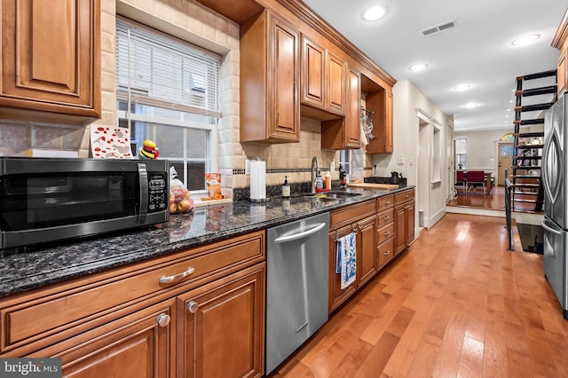 kitchen featuring dark stone countertops, tasteful backsplash, light wood-type flooring, and appliances with stainless steel finishes