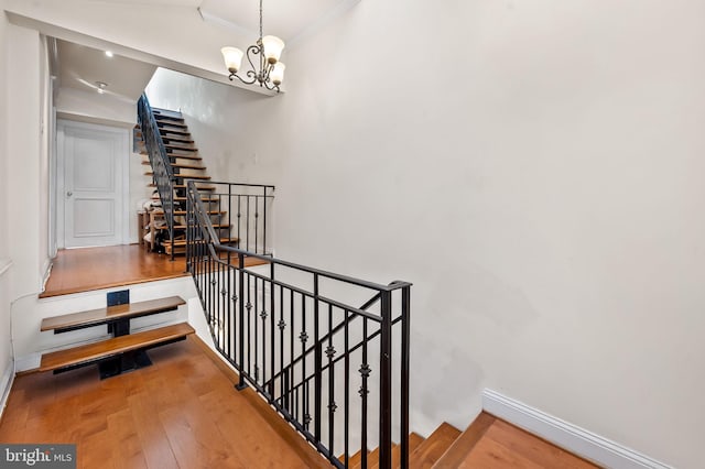 stairs featuring hardwood / wood-style flooring, crown molding, and a notable chandelier