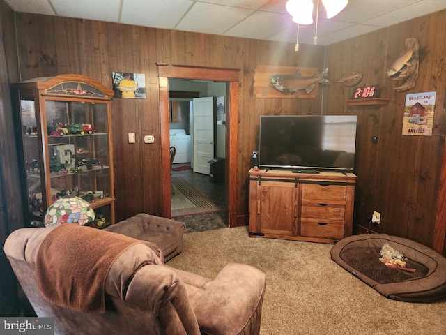 living room with wooden walls, washer / dryer, carpet floors, a drop ceiling, and ceiling fan