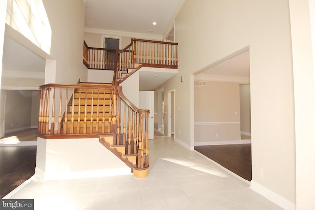 staircase with wood-type flooring, ornamental molding, and a high ceiling