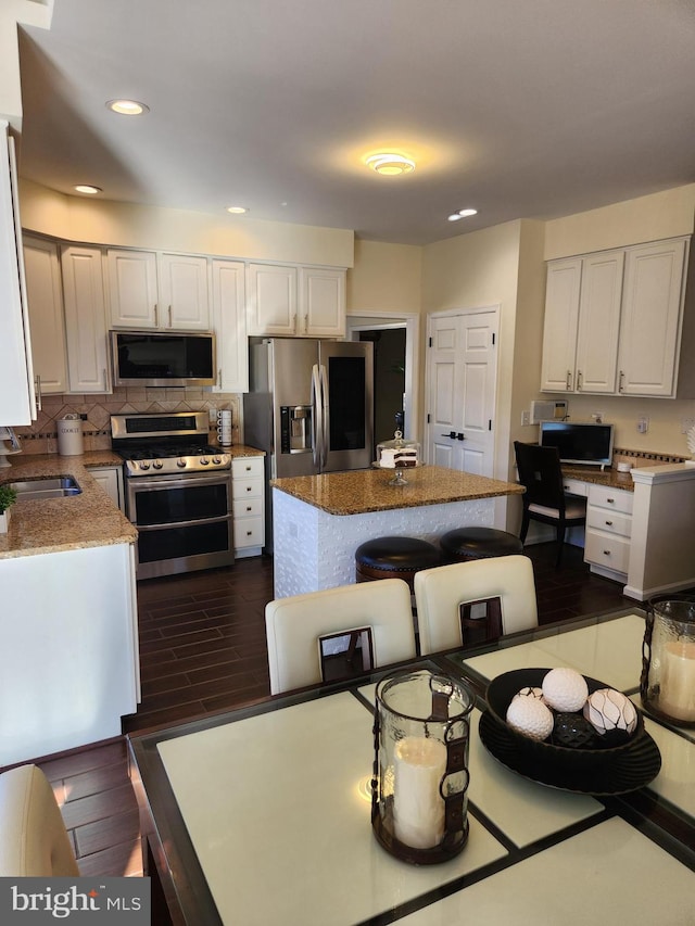 kitchen featuring stainless steel appliances, white cabinetry, dark hardwood / wood-style floors, sink, and a center island