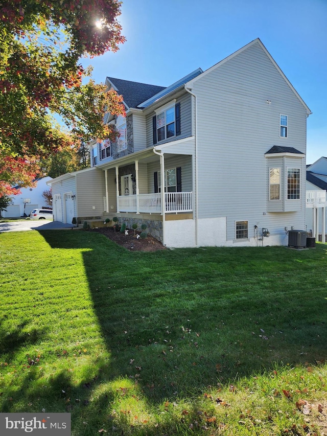 view of side of home featuring a garage, cooling unit, covered porch, and a yard