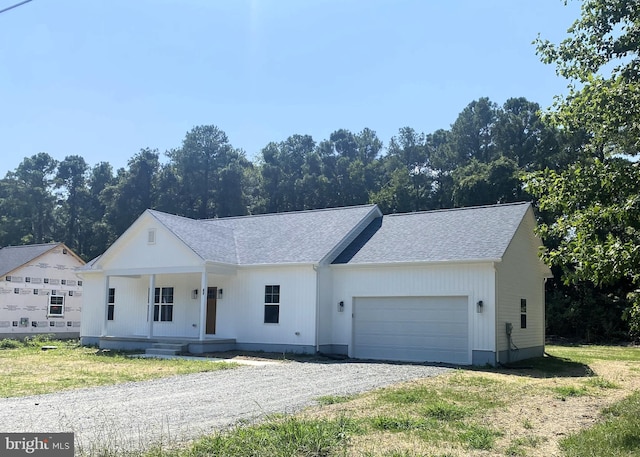 view of front facade featuring a garage, a porch, gravel driveway, and a shingled roof