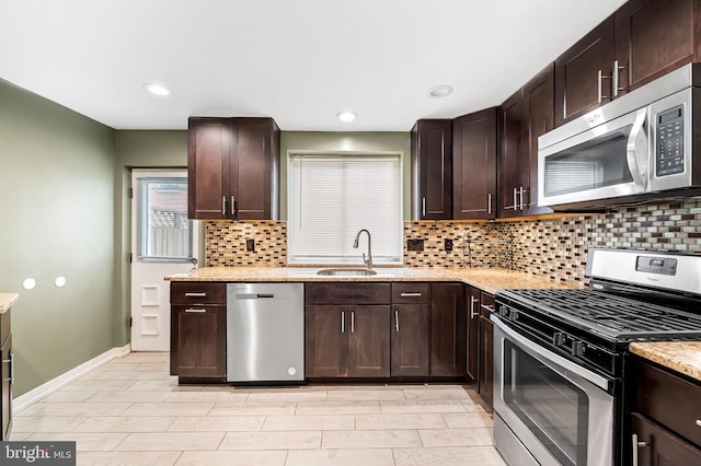 kitchen featuring light stone countertops, tasteful backsplash, dark brown cabinets, stainless steel appliances, and sink