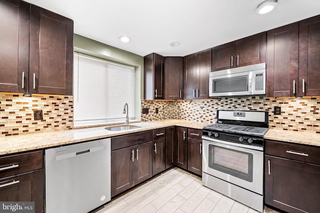 kitchen with light stone countertops, backsplash, dark brown cabinets, stainless steel appliances, and sink