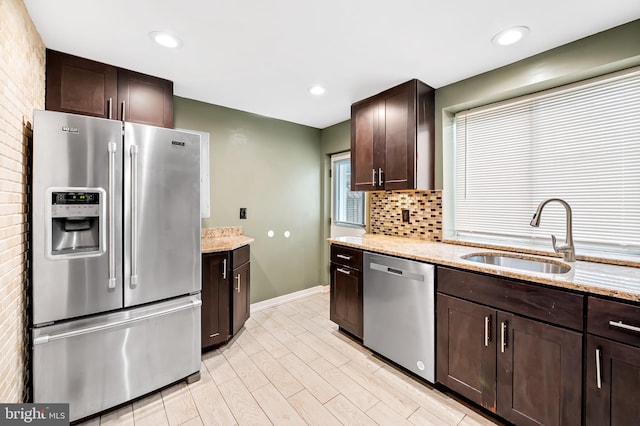 kitchen with sink, stainless steel appliances, light stone counters, light hardwood / wood-style floors, and dark brown cabinets