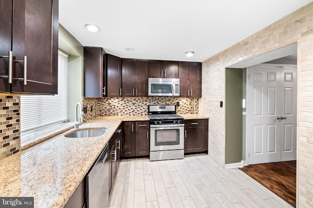 kitchen featuring sink, light stone countertops, appliances with stainless steel finishes, light hardwood / wood-style floors, and dark brown cabinetry