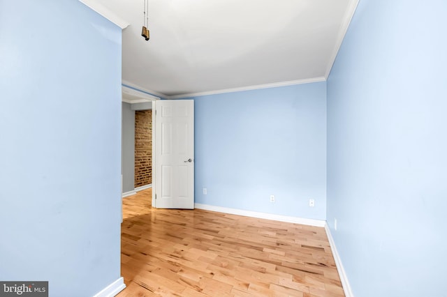 unfurnished room featuring ornamental molding, brick wall, and light hardwood / wood-style flooring