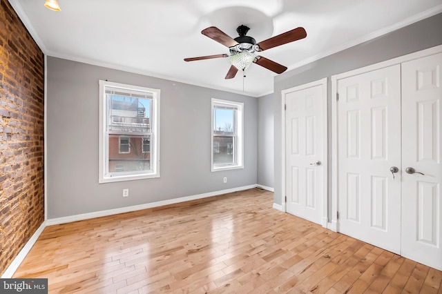 unfurnished bedroom with ceiling fan, light hardwood / wood-style floors, crown molding, and brick wall