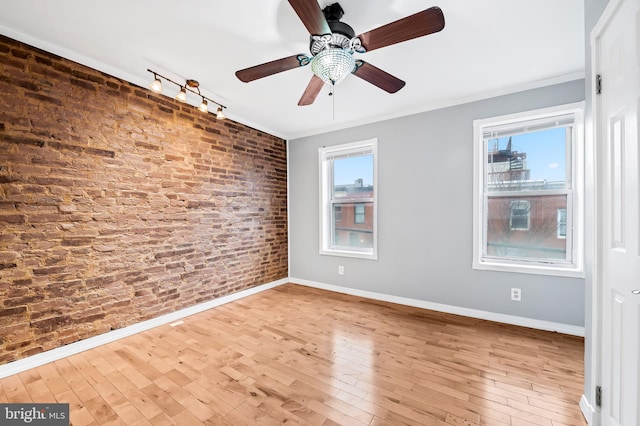 spare room with hardwood / wood-style flooring, ornamental molding, rail lighting, and brick wall