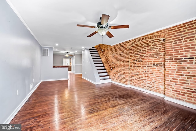 unfurnished living room featuring crown molding, ceiling fan, wood-type flooring, and brick wall