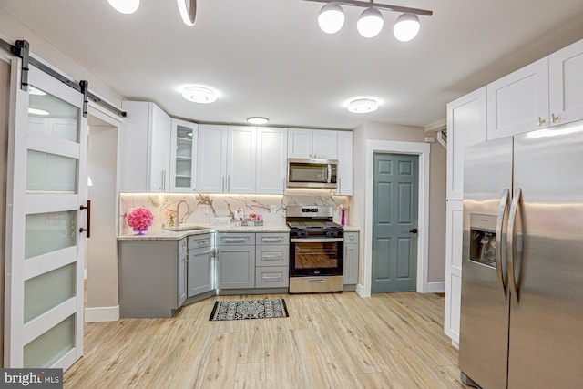 kitchen with decorative backsplash, stainless steel appliances, a barn door, and light wood-type flooring