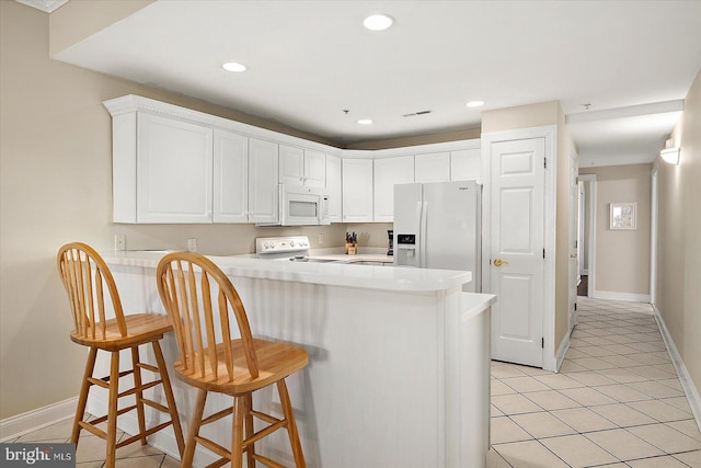 kitchen featuring white cabinets, kitchen peninsula, white appliances, a breakfast bar area, and light tile patterned floors