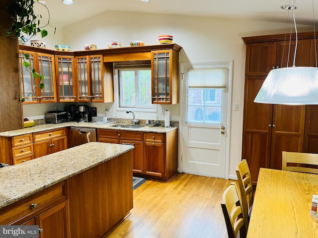 kitchen with lofted ceiling, sink, stainless steel dishwasher, light wood-type flooring, and light stone counters