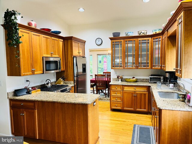 kitchen with light stone countertops, sink, stainless steel appliances, kitchen peninsula, and light hardwood / wood-style floors