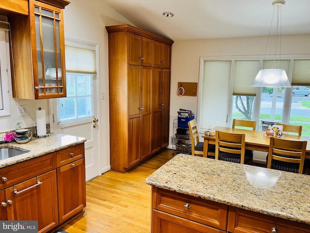 kitchen with pendant lighting, a healthy amount of sunlight, light stone counters, and light wood-type flooring