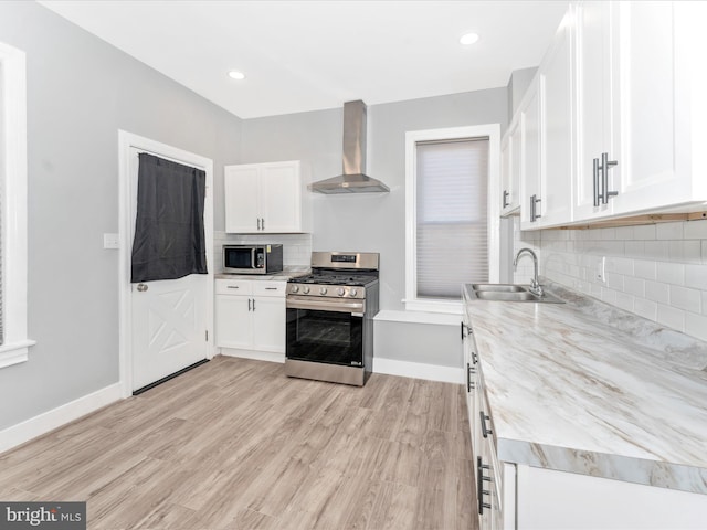 kitchen featuring stainless steel appliances, white cabinetry, sink, wall chimney exhaust hood, and light hardwood / wood-style flooring