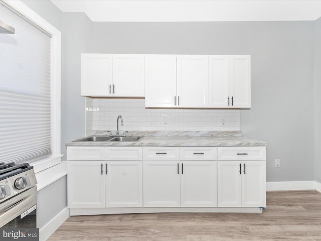 kitchen featuring stainless steel stove, light hardwood / wood-style floors, white cabinetry, and sink