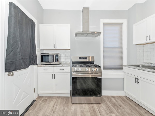 kitchen with stainless steel appliances, light hardwood / wood-style floors, white cabinets, decorative backsplash, and wall chimney exhaust hood