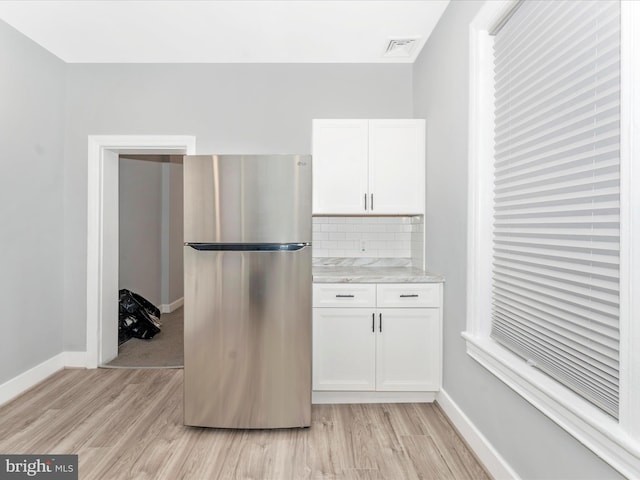 kitchen with stainless steel refrigerator, white cabinetry, light hardwood / wood-style flooring, and decorative backsplash