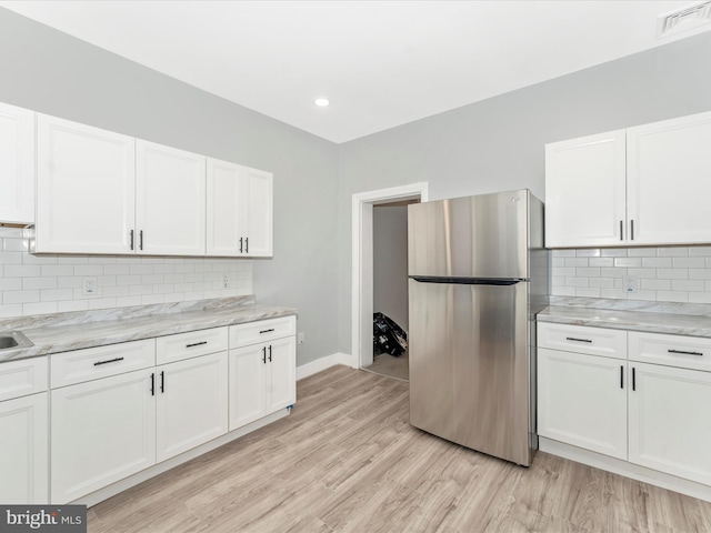 kitchen with stainless steel refrigerator, white cabinetry, light hardwood / wood-style flooring, and decorative backsplash