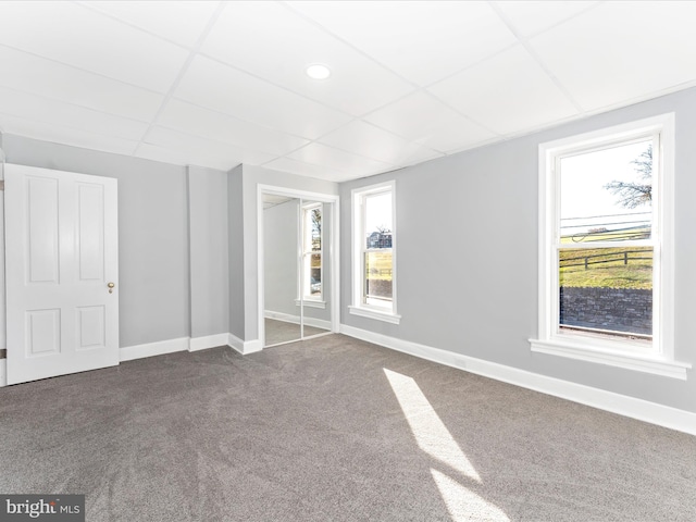 unfurnished bedroom featuring carpet, a paneled ceiling, multiple windows, and a closet