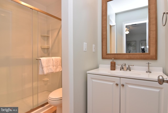 bathroom with toilet, vanity, a shower with door, and ceiling fan