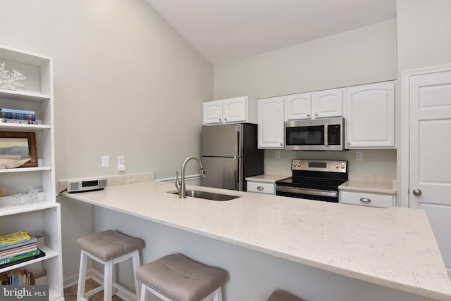 kitchen with stainless steel appliances, sink, vaulted ceiling, white cabinets, and kitchen peninsula