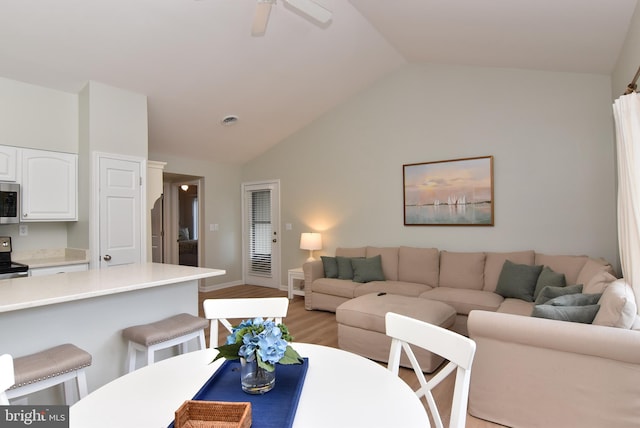 living room with ceiling fan, vaulted ceiling, and light hardwood / wood-style floors