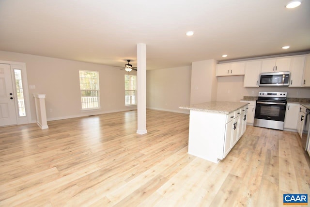 kitchen with light stone counters, stainless steel appliances, white cabinetry, light hardwood / wood-style flooring, and a kitchen island