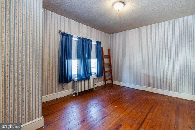 unfurnished room featuring a textured ceiling, radiator heating unit, and dark hardwood / wood-style flooring