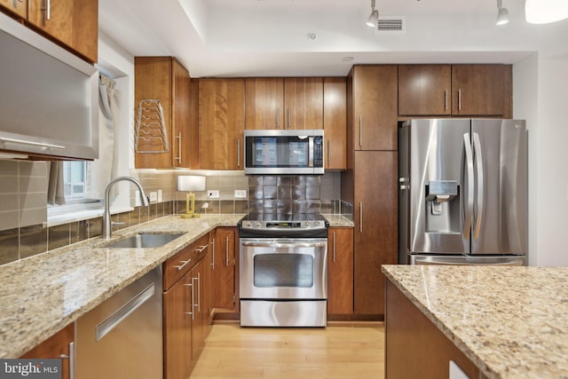 kitchen with tasteful backsplash, appliances with stainless steel finishes, sink, and light stone counters