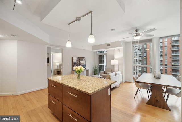 kitchen with light hardwood / wood-style flooring, a kitchen island, pendant lighting, ceiling fan, and light stone countertops