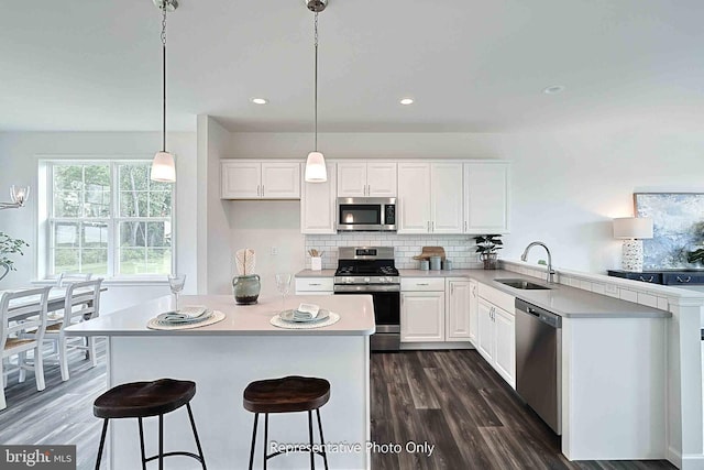 kitchen with dark wood-type flooring, pendant lighting, sink, white cabinetry, and appliances with stainless steel finishes